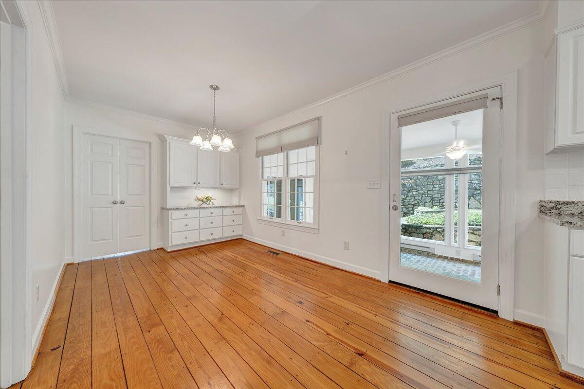 Unfurnished dining room with wide-plank hardwood floors, white built-ins, and a glass door to a sunroom.