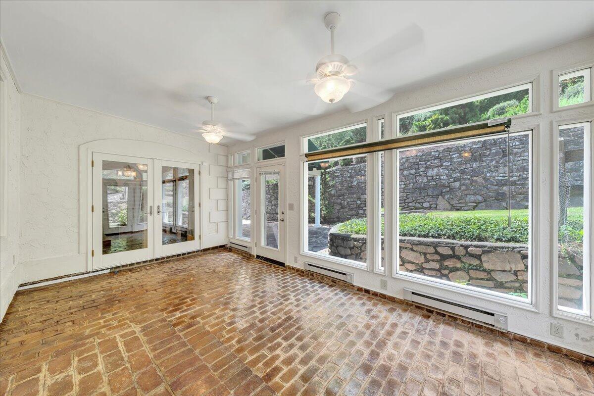 Vacant sunroom with a brick floor and large windows overlooking a stone wall and garden.