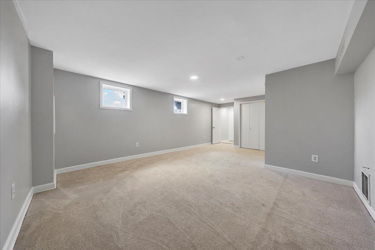 Empty carpeted room with gray walls, two high windows, and doors at the far end.