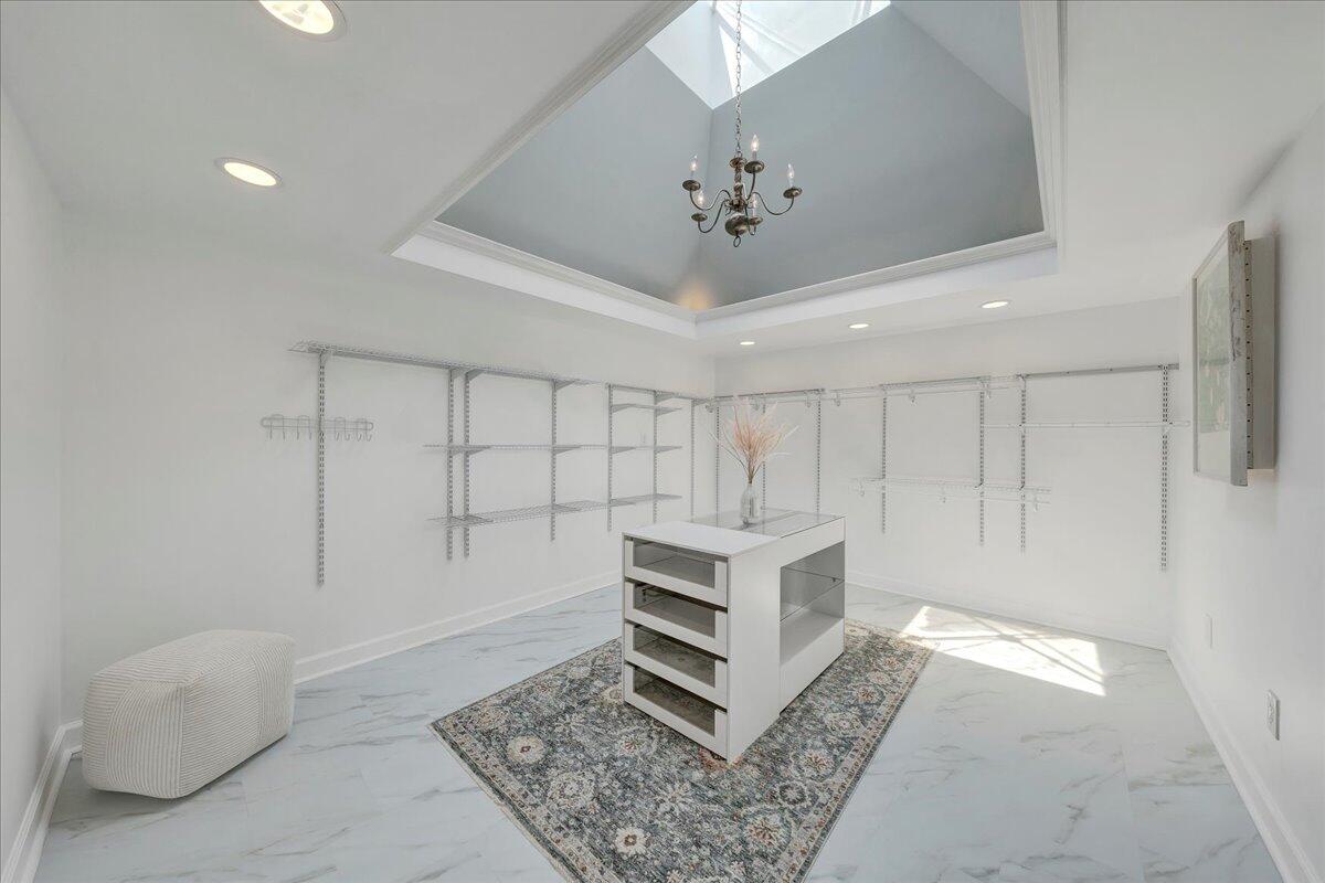 Walk-in closet with open shelving, a central drawer island, patterned rug, and tray ceiling.