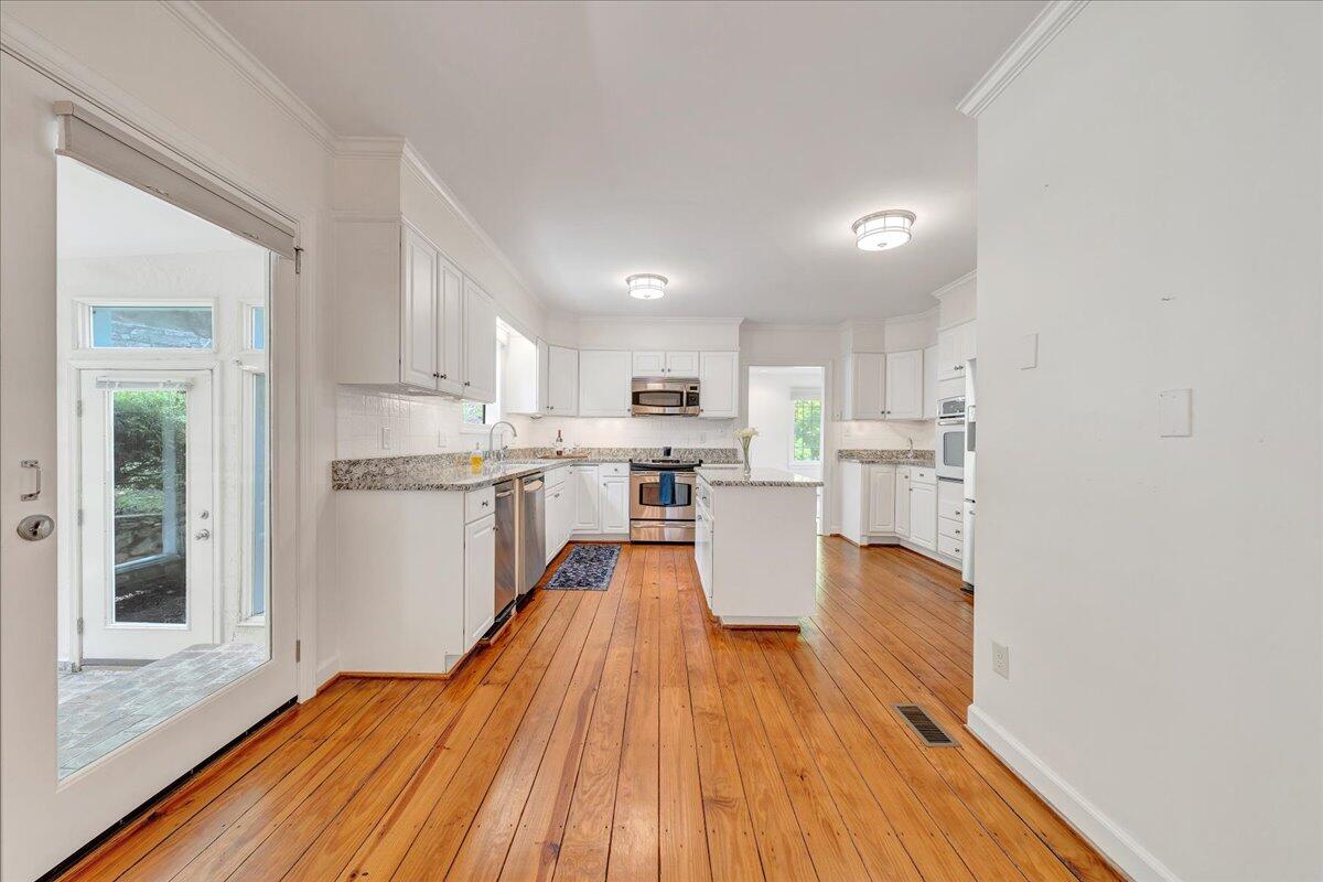 Kitchen with white cabinets, stainless steel appliances, a central island, and warm hardwood floors.