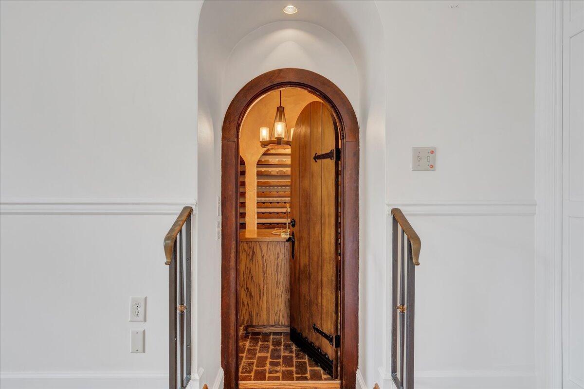Arched wooden doorway opens into a wine cellar with wooden racks and a brick floor.