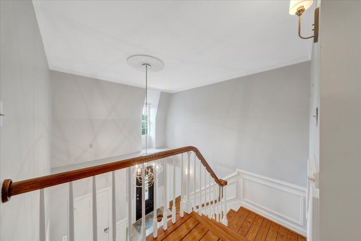 Two-story stair hall with polished hardwood stairs, white balusters, and a hanging chandelier.