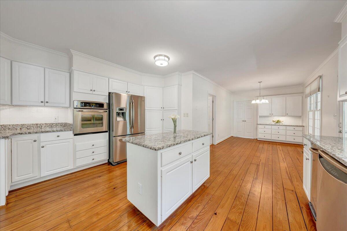 Kitchen with white cabinets, stainless steel appliances, granite island, and hardwood floors opening to a dining area.