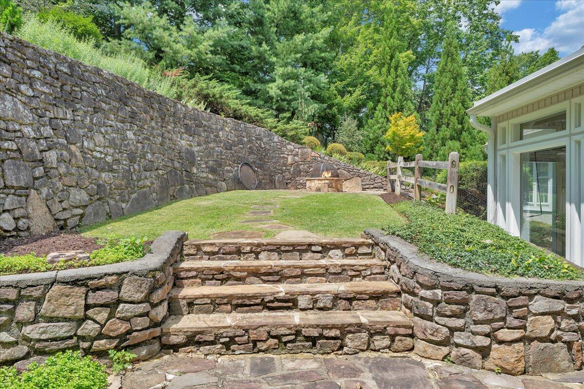 Backyard terrace with broad stone steps, a tall retaining wall, and a small fire pit.