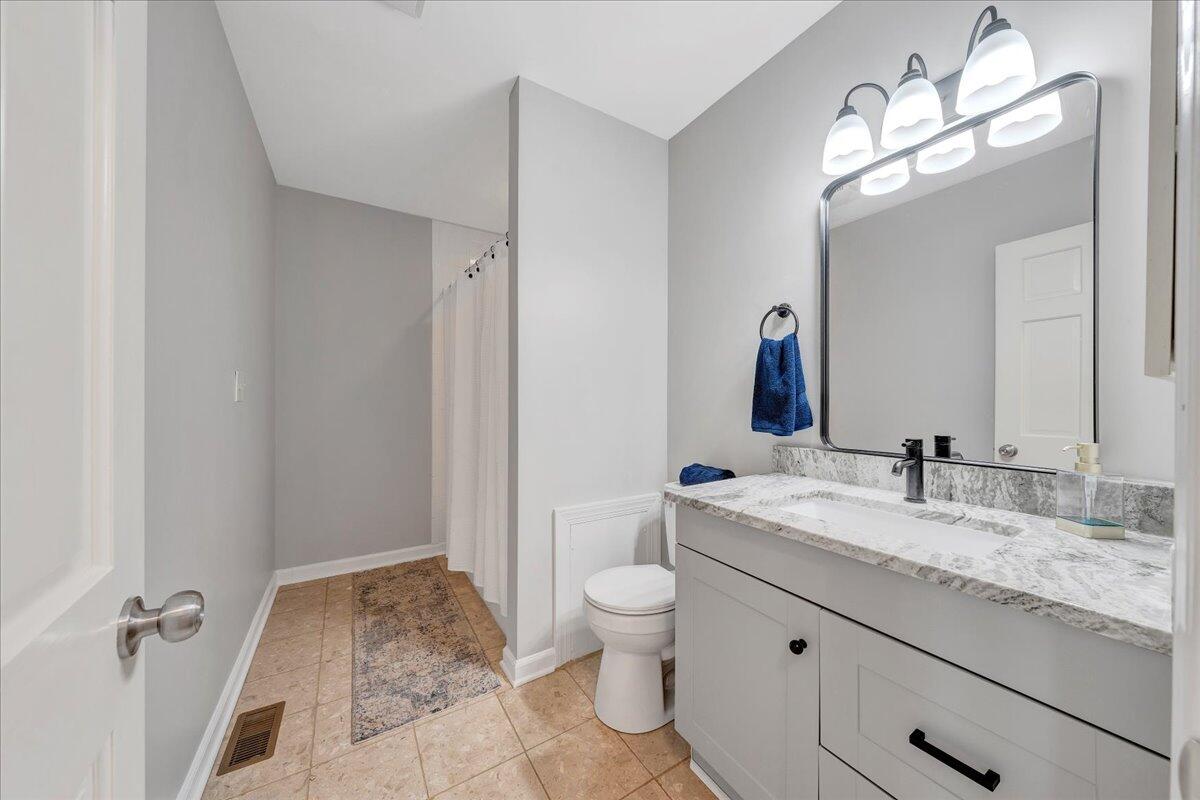 Bathroom with a white vanity, marble-look counter, large mirror, and tiled floor.