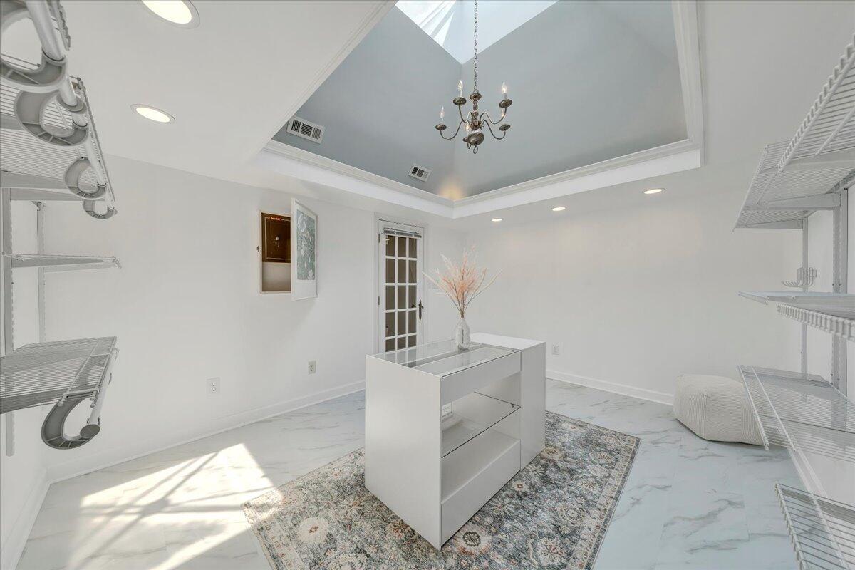 Walk-in closet with white wire shelving, a glass-topped island, and a skylit tray ceiling.