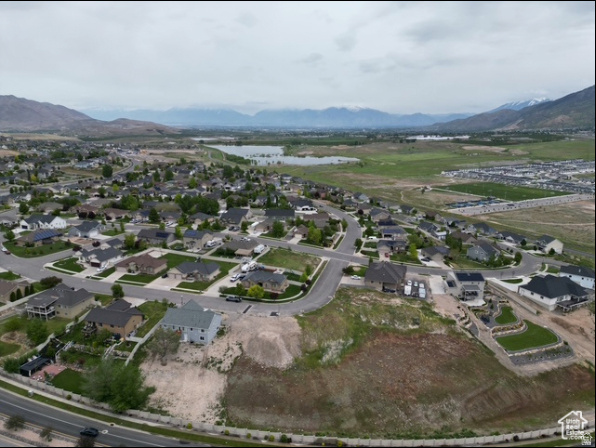 Aerial view of a residential neighborhood, with an undeveloped foreground lot, distant lake, and mountain range.