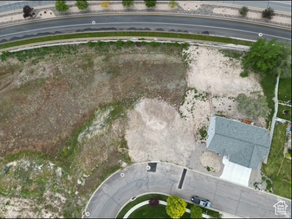 Aerial view of a mostly bare lot with a house beside a curved residential street.