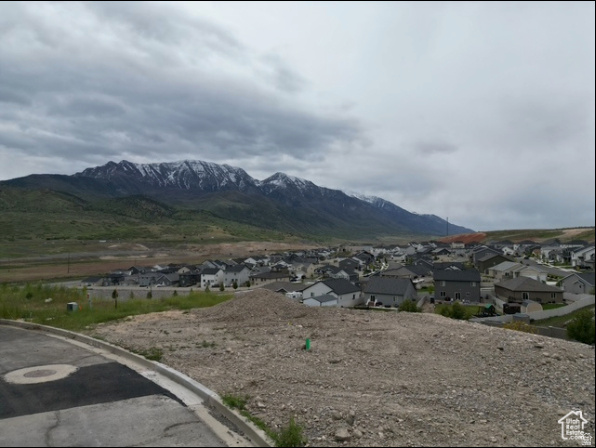 Vacant lot overlooking a neighborhood and snow-dusted mountains under cloudy skies.