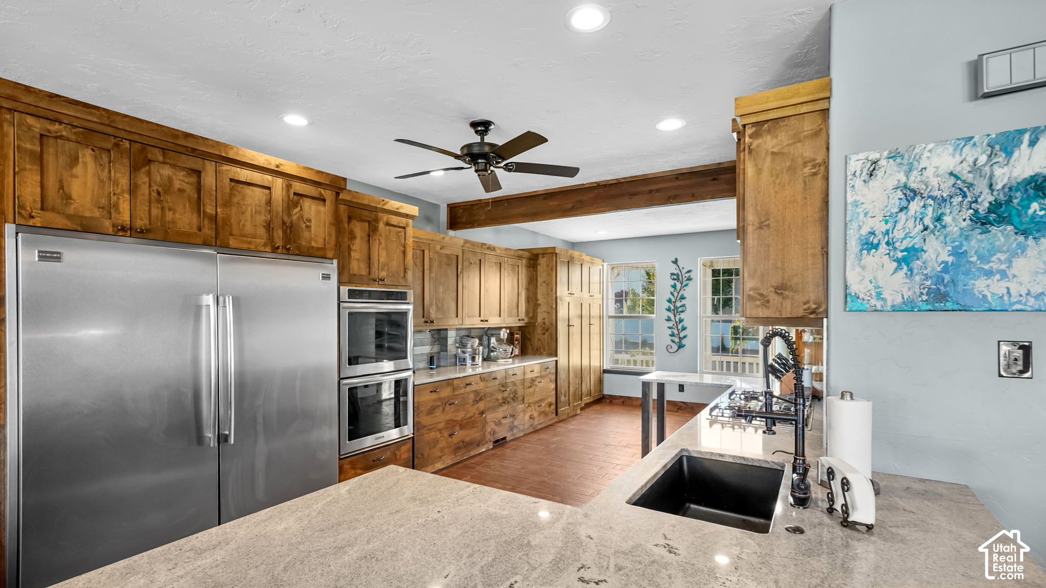 Kitchen with warm wood cabinets, stainless appliances, and a large stone island with sink and cooktop.
