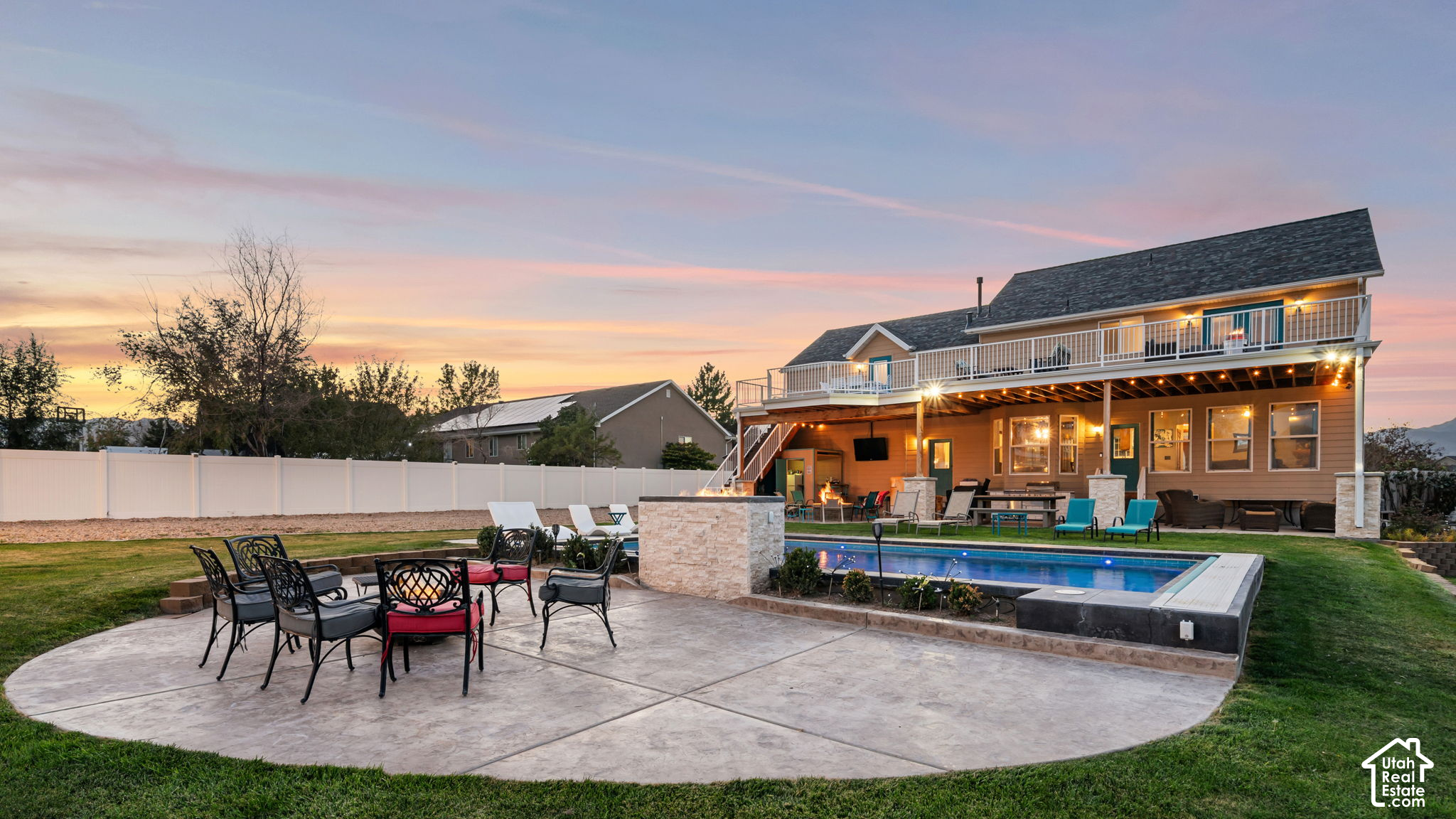 Backyard with a swimming pool, curved patio, covered outdoor seating area, and long upper deck at dusk.