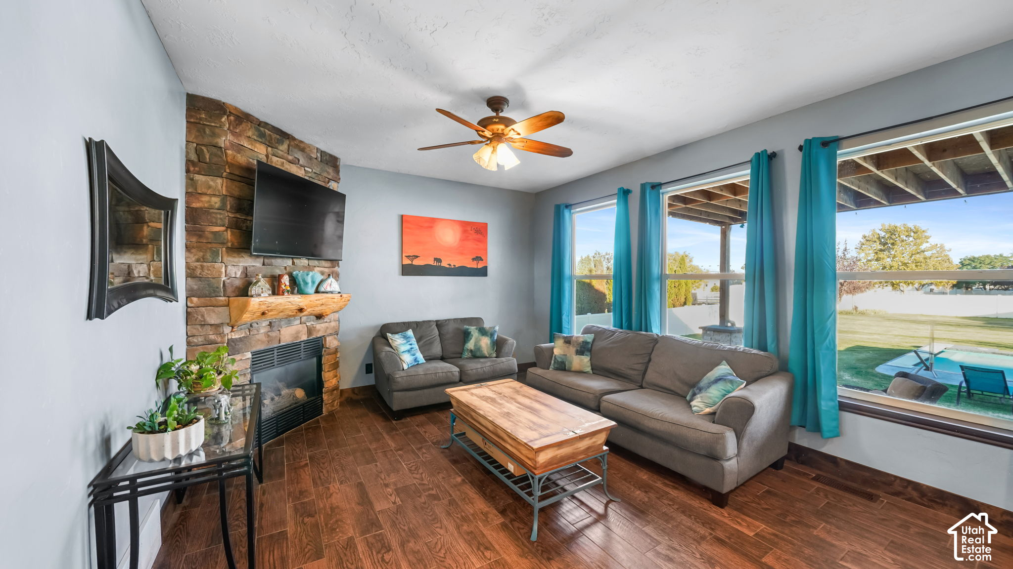 Living room with a stone fireplace, gray sofas, and bright windows overlooking the backyard pool.