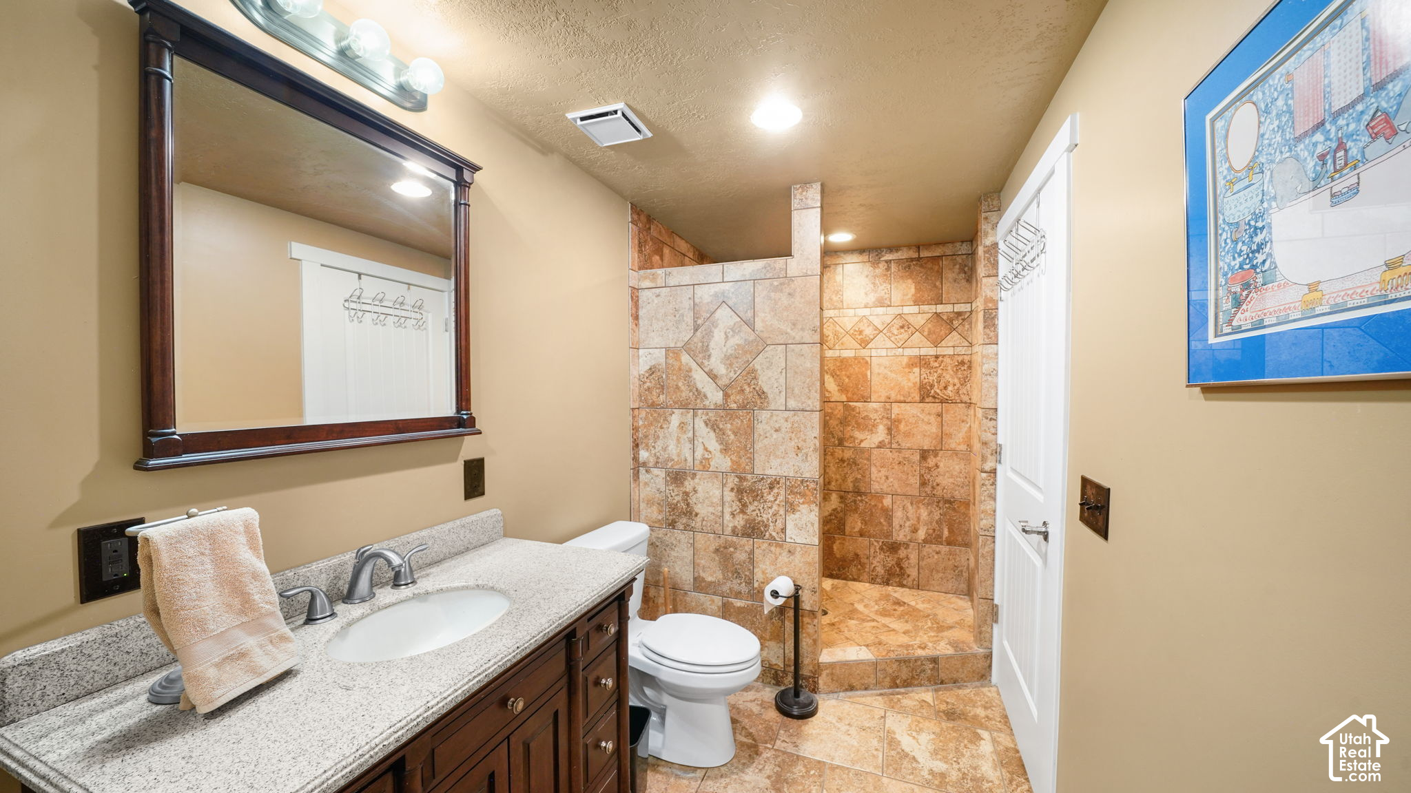 Bathroom with a dark wood vanity and a walk-in shower tiled in patterned tan stone.