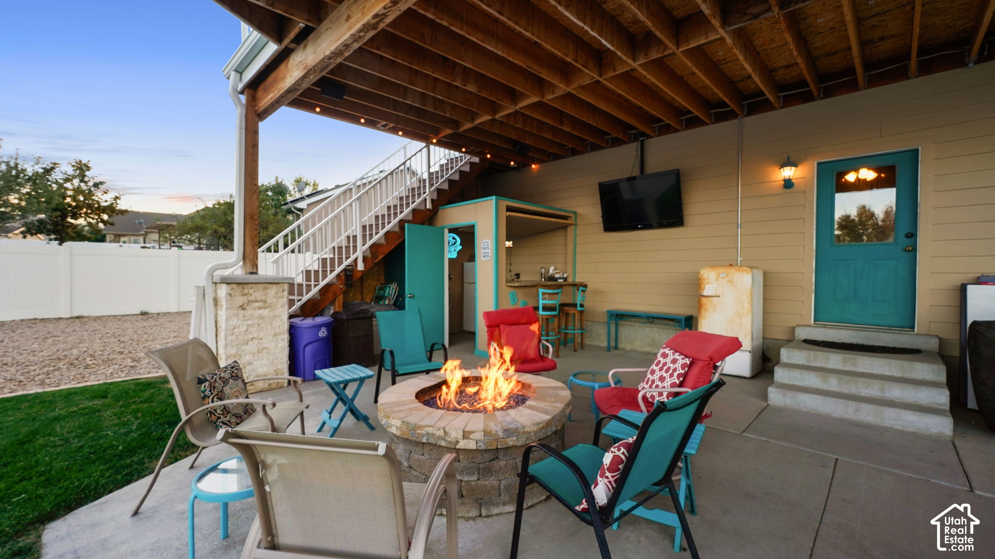 Covered backyard patio with a stone fire pit, colorful chairs, and stairs to the upper deck.