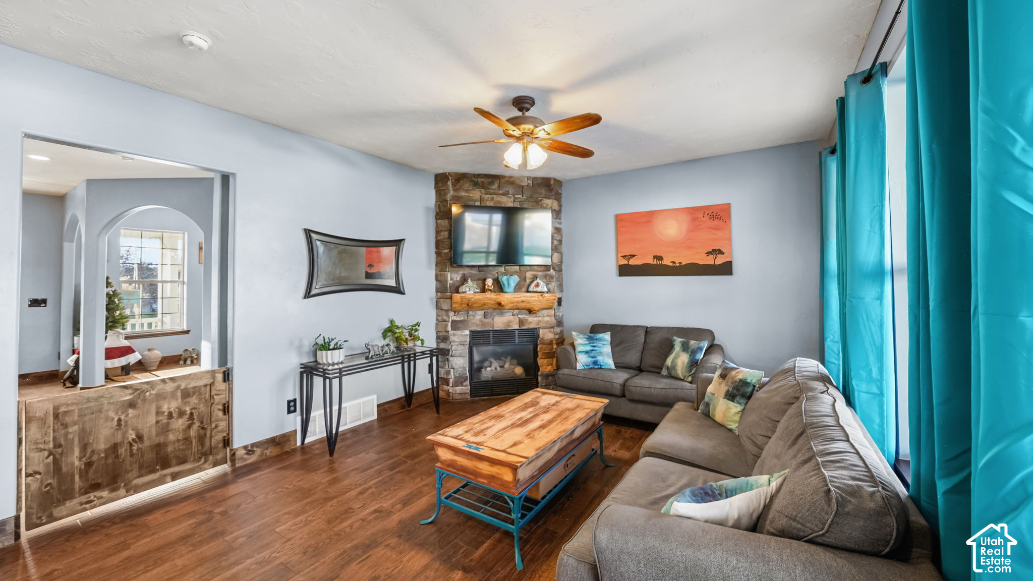 Living room with stone fireplace, gray sectional, wood coffee table, and turquoise curtains.