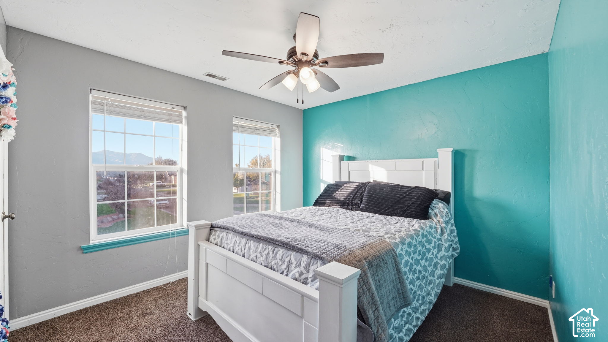 Bedroom with a white bed, teal accent wall, and mountain views through two windows.