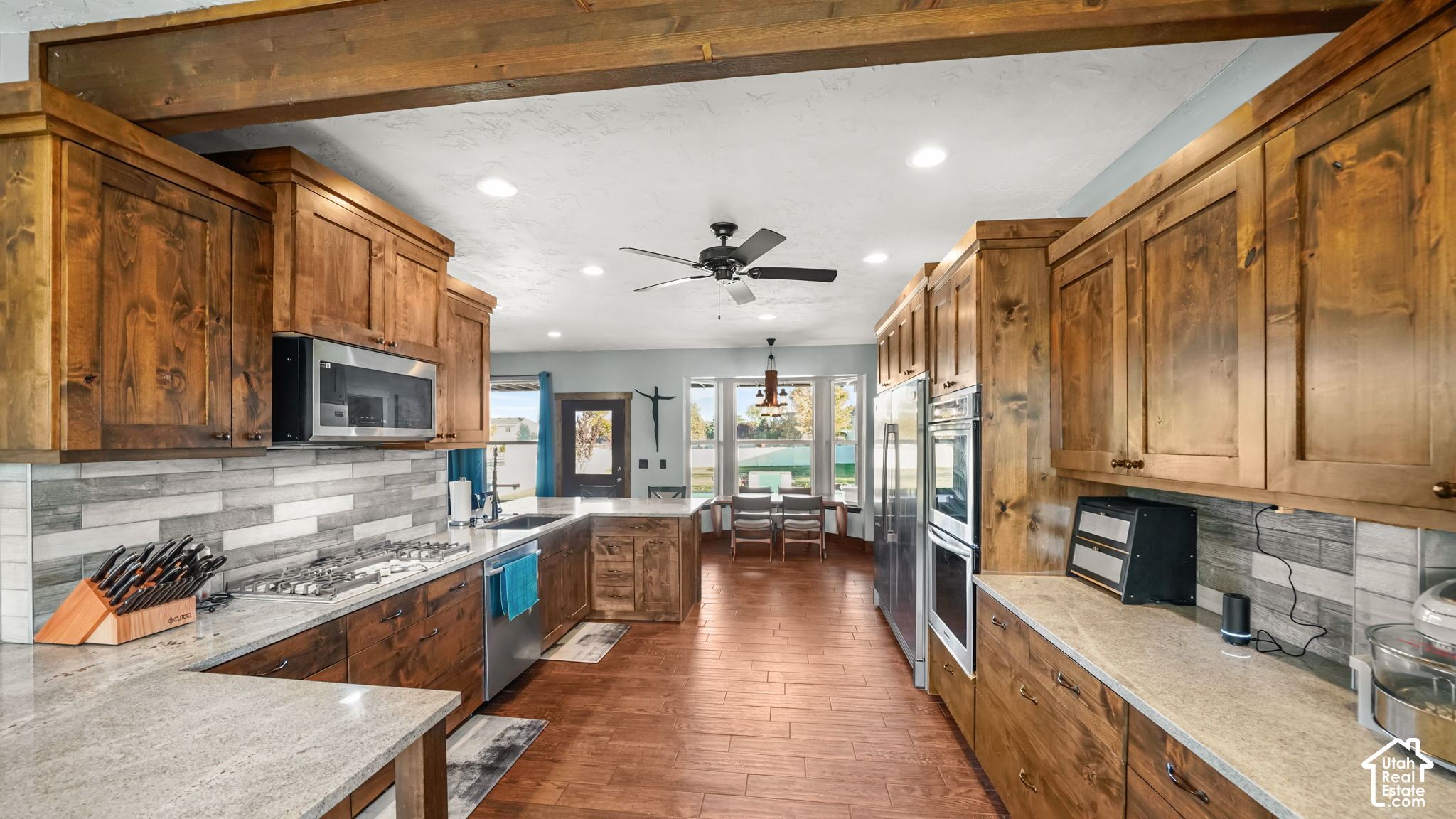 Kitchen with warm wood cabinetry, stone counters, stainless appliances, and a dining area by the windows.