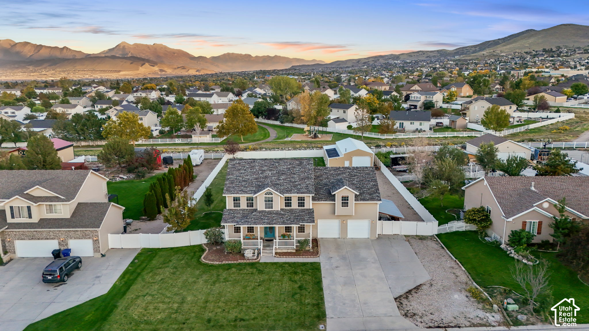Aerial view of a two-story home with a fenced yard, backed by a suburban neighborhood and mountain range.