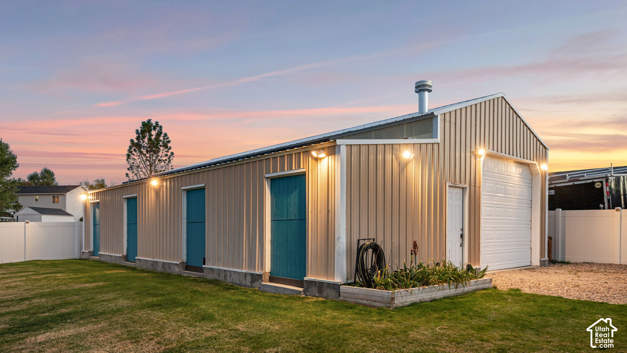Large metal outbuilding with teal doors, a white garage door, and exterior lights at sunset.