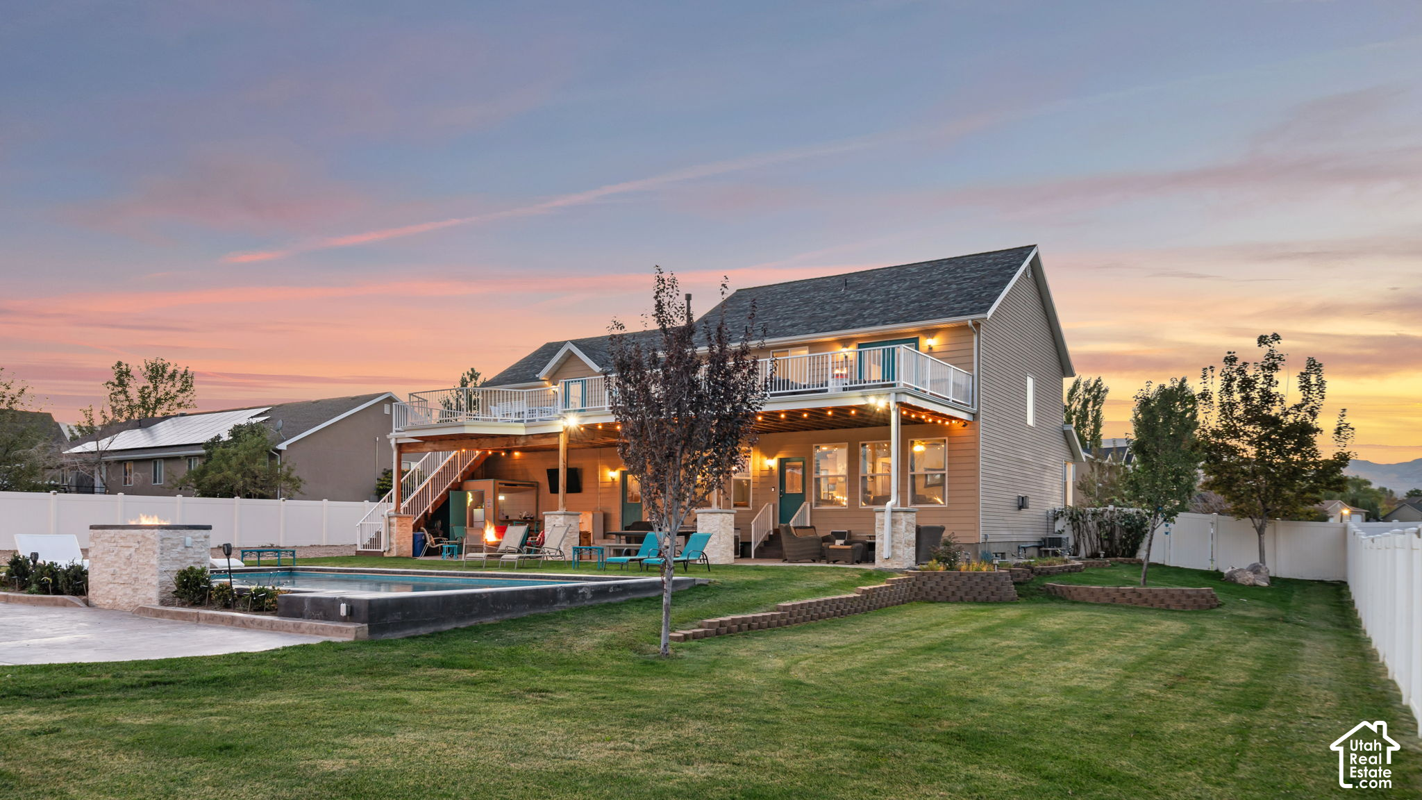 Home’s backyard at dusk, with a raised deck, swimming pool, and white fencing.