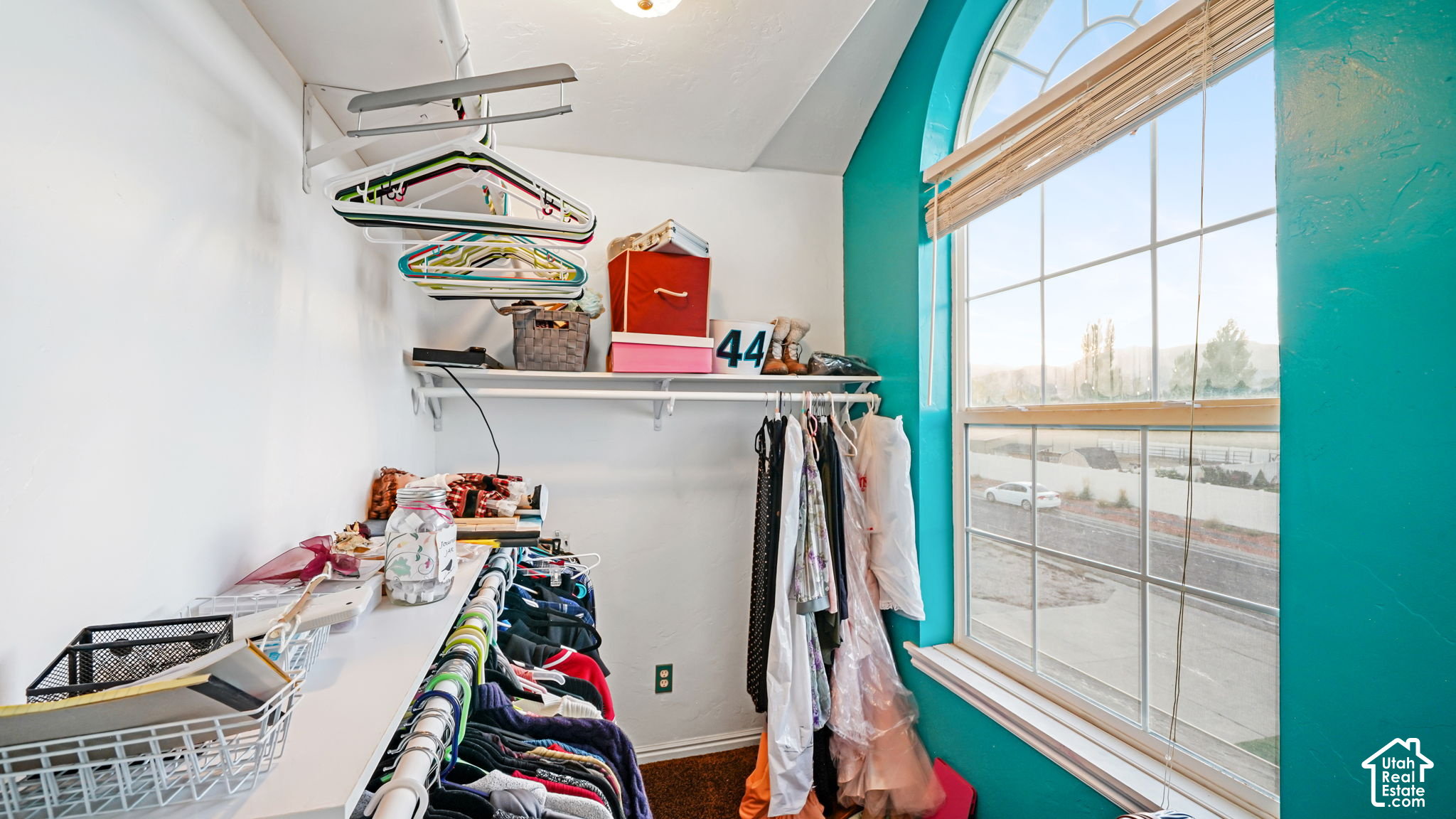 Walk-in closet with crowded clothing racks and a tall arched window framed in turquoise.