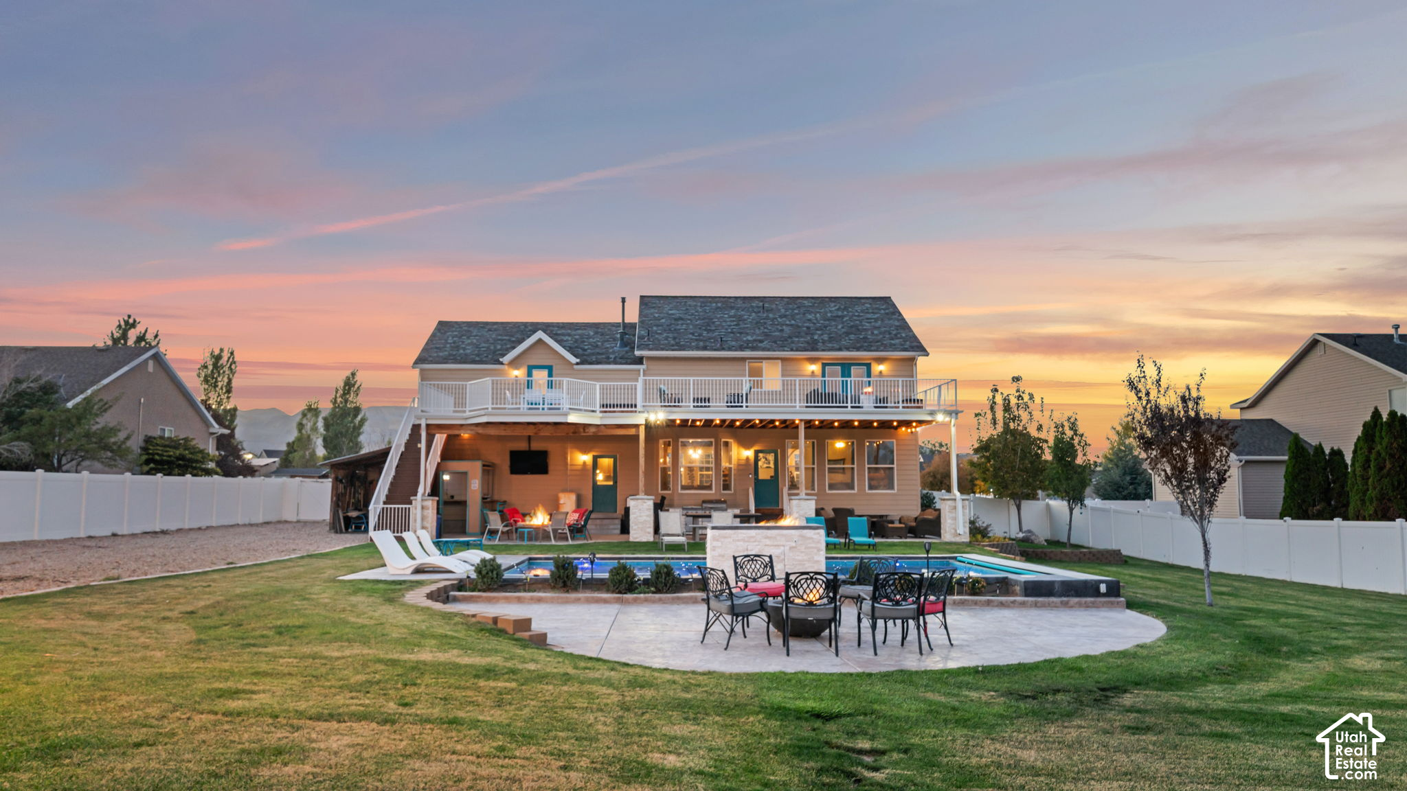 Two-story home with an elevated deck, swimming pool, and patio seating at sunset.
