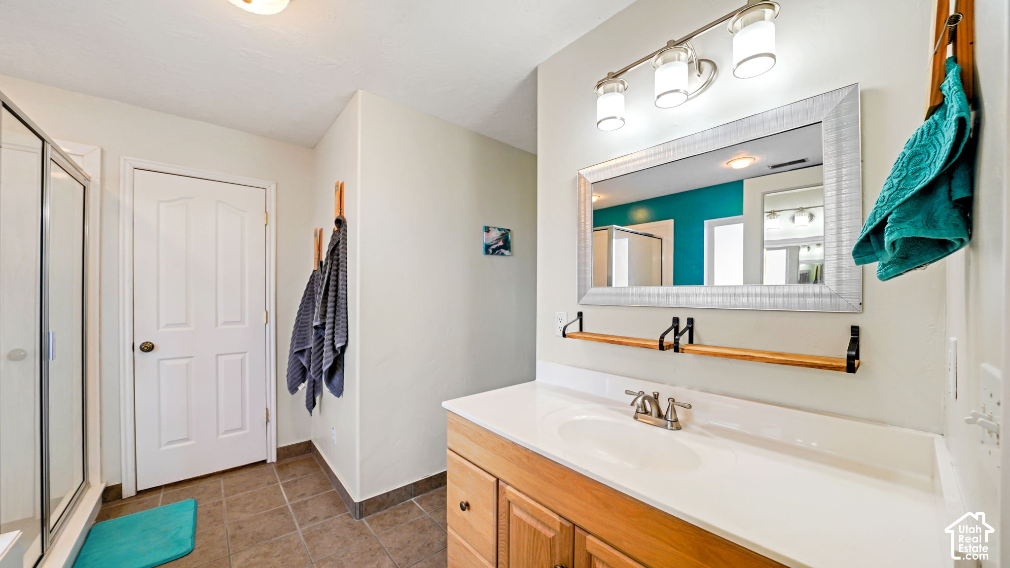 Bathroom with a wood vanity, large mirror, glass shower, and teal towels and bath mat.