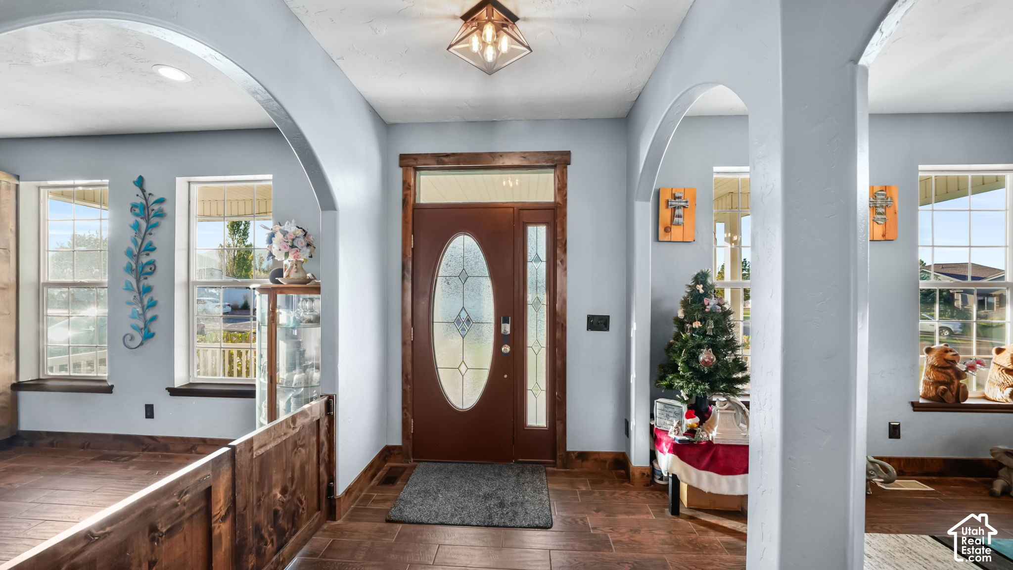 Home entryway with arched openings, a brown oval-glass front door, and wood-look tile flooring.