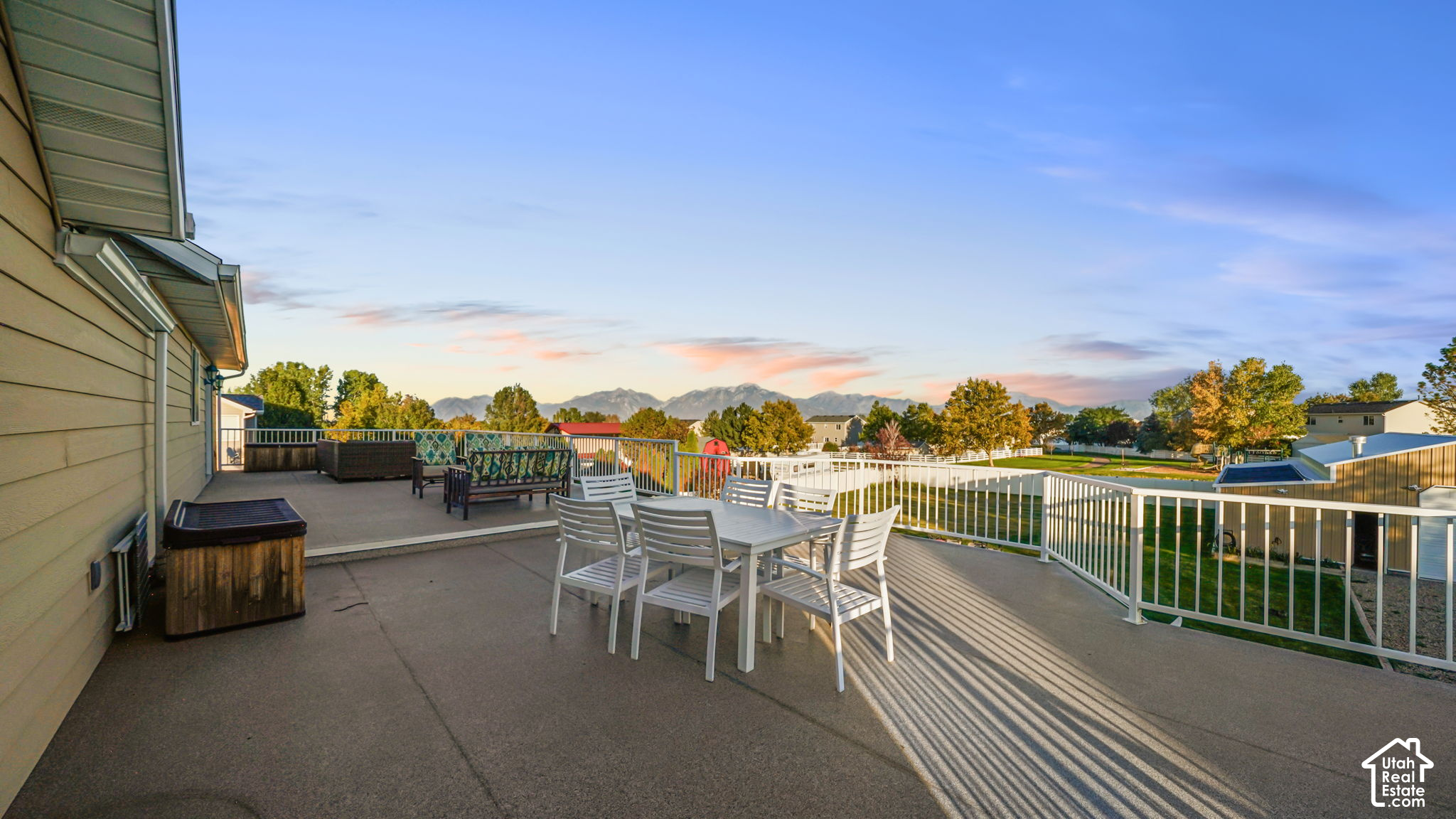 Furnished deck with outdoor dining set and hot tub overlooking a yard and mountain range.