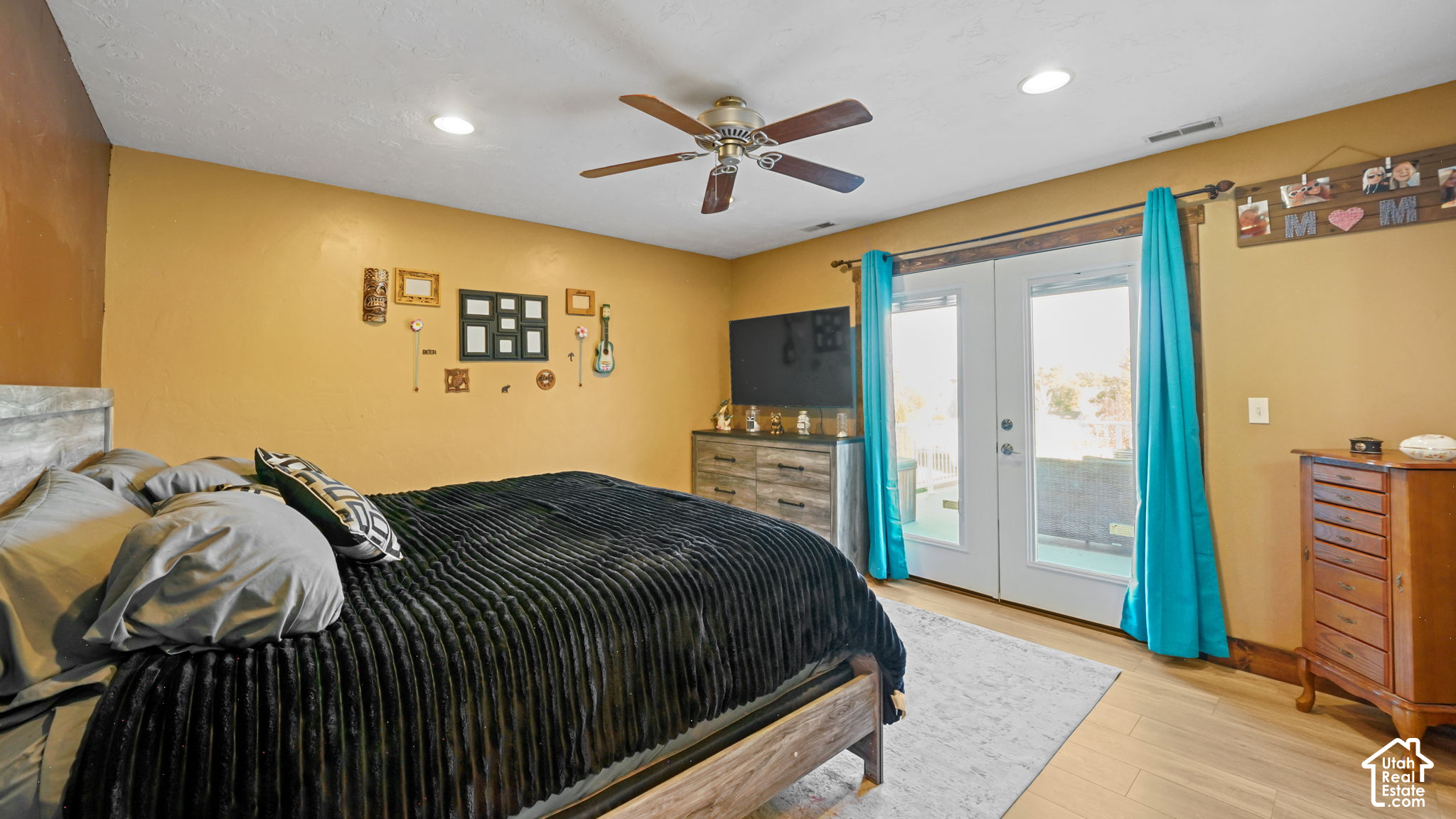 Bedroom with a large dark-quilted bed, ceiling fan, and patio doors with turquoise curtains.