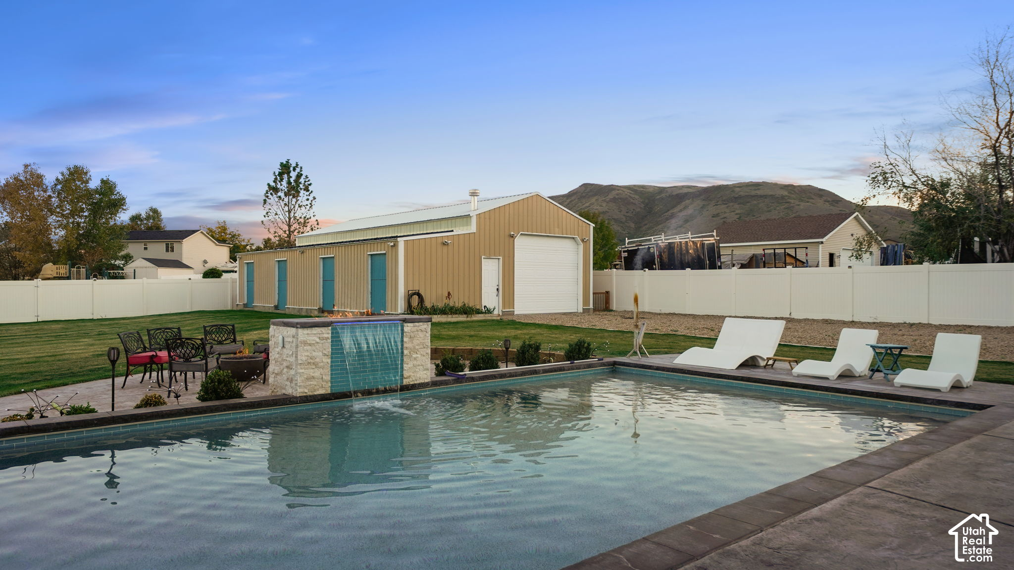 Backyard pool with a tiled waterfall feature, patio loungers, and foothills beyond the fence.