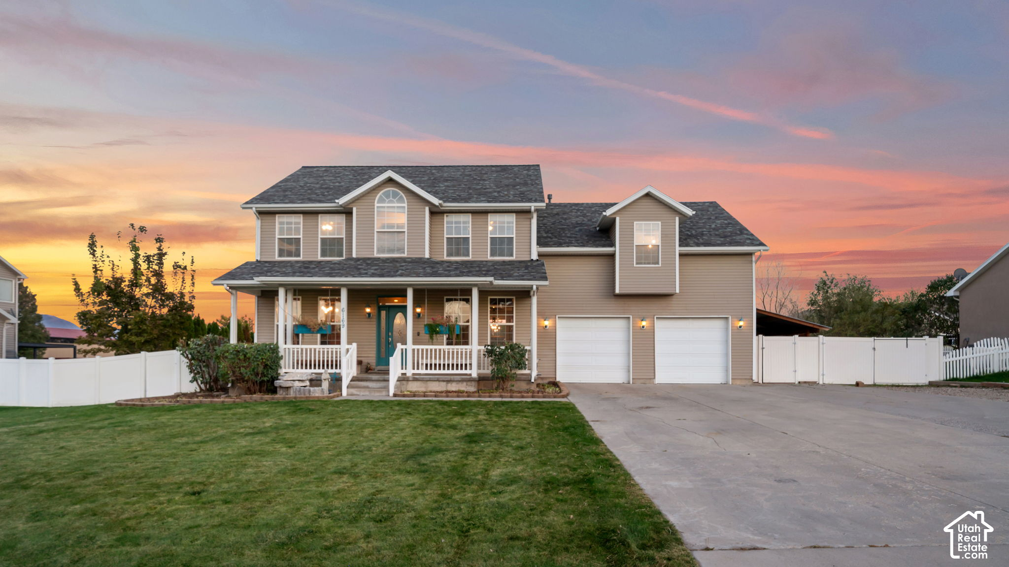 Two-story beige home with a covered porch and two-car garage at sunset.