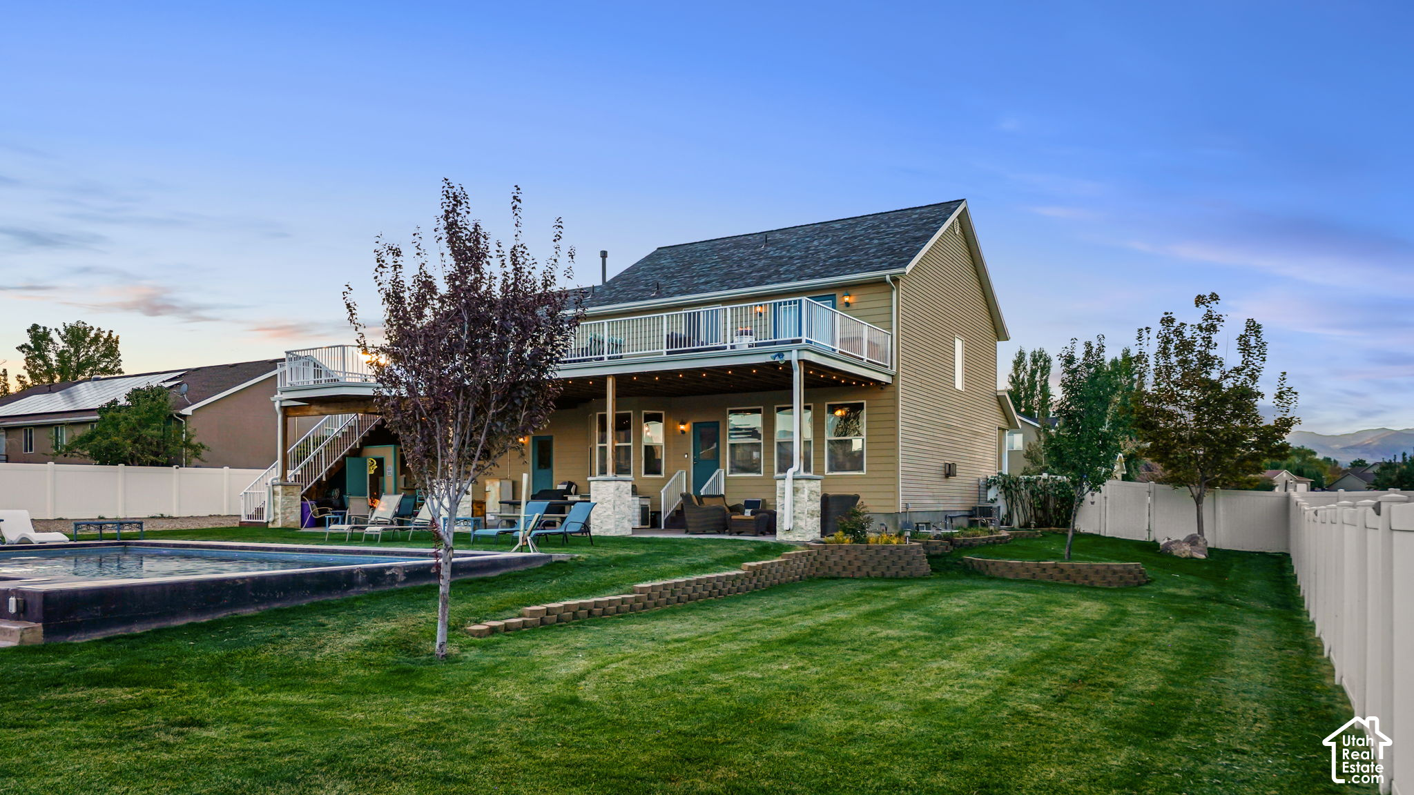 Home’s rear exterior with a raised deck, covered patio, swimming pool, and fenced lawn.