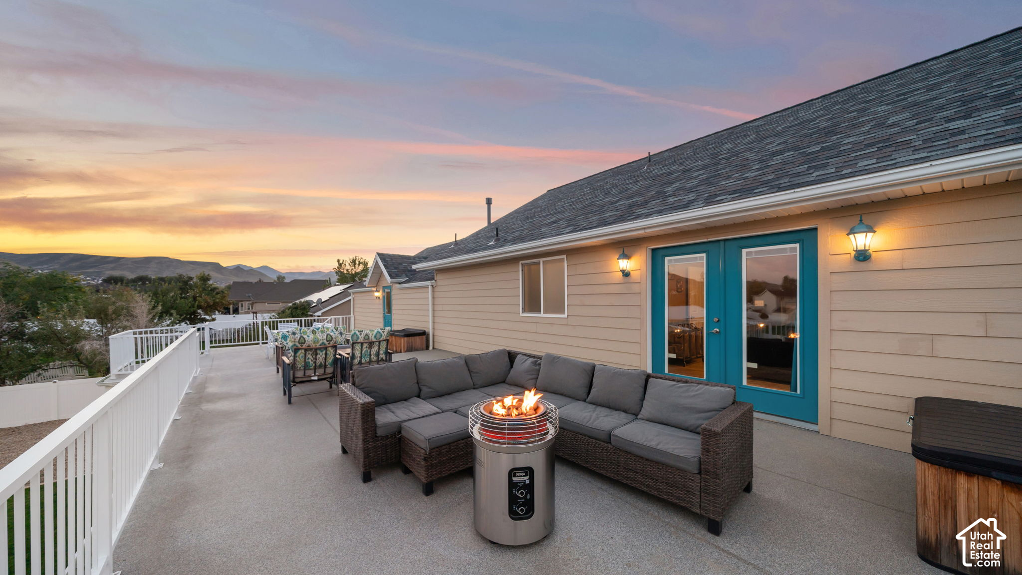 Raised patio with a sectional sofa and lit fire pit overlooking mountains at sunset.