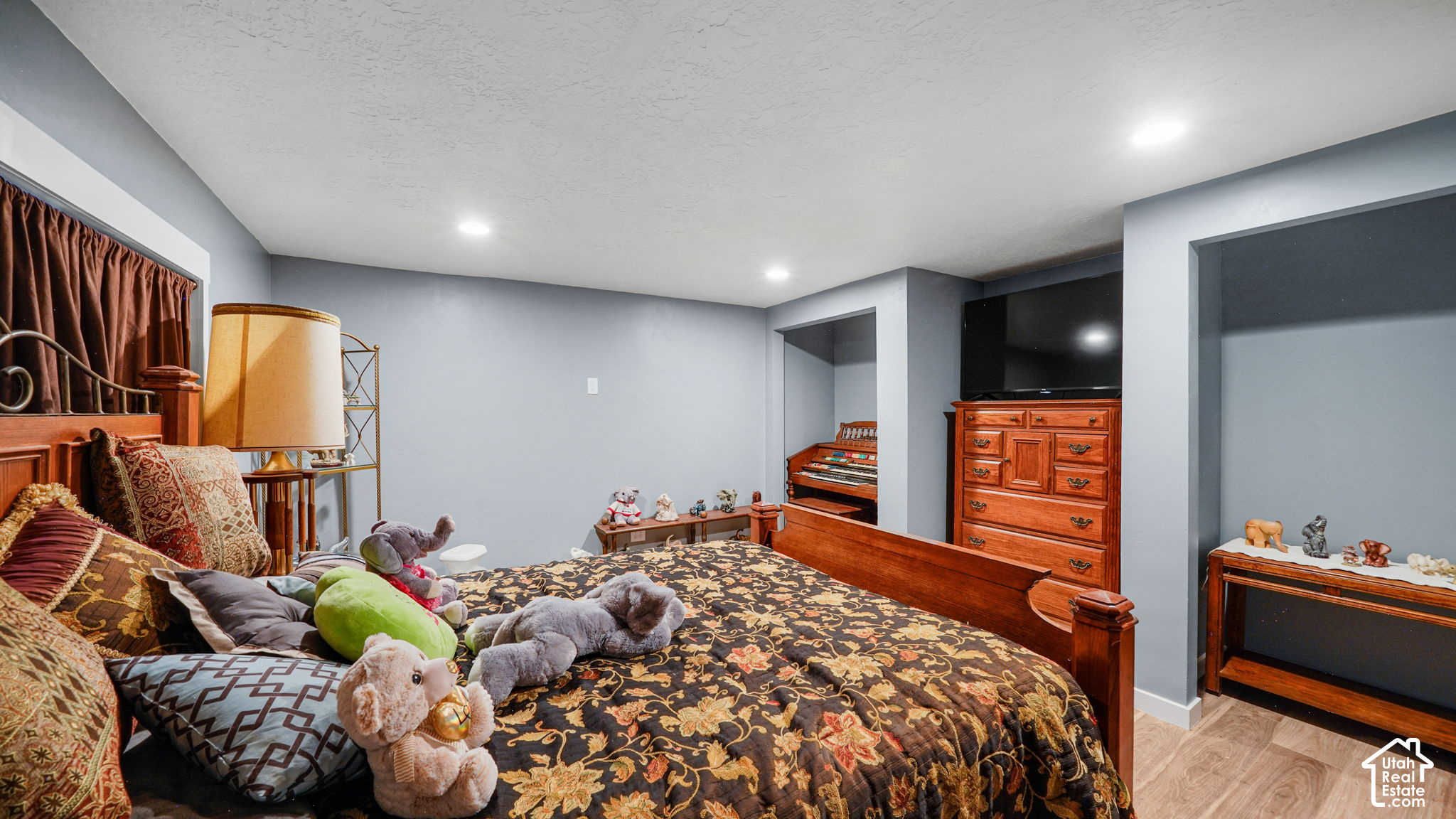 Furnished bedroom with a patterned bed, wooden dresser and television, and a keyboard in a wall nook.