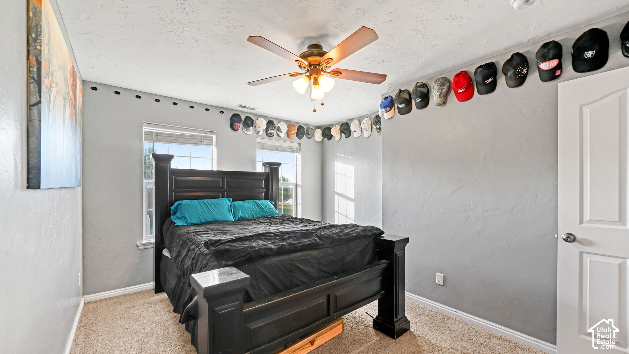 Bedroom with a dark four-poster bed, turquoise pillows, ceiling fan, and baseball caps displayed along the walls.