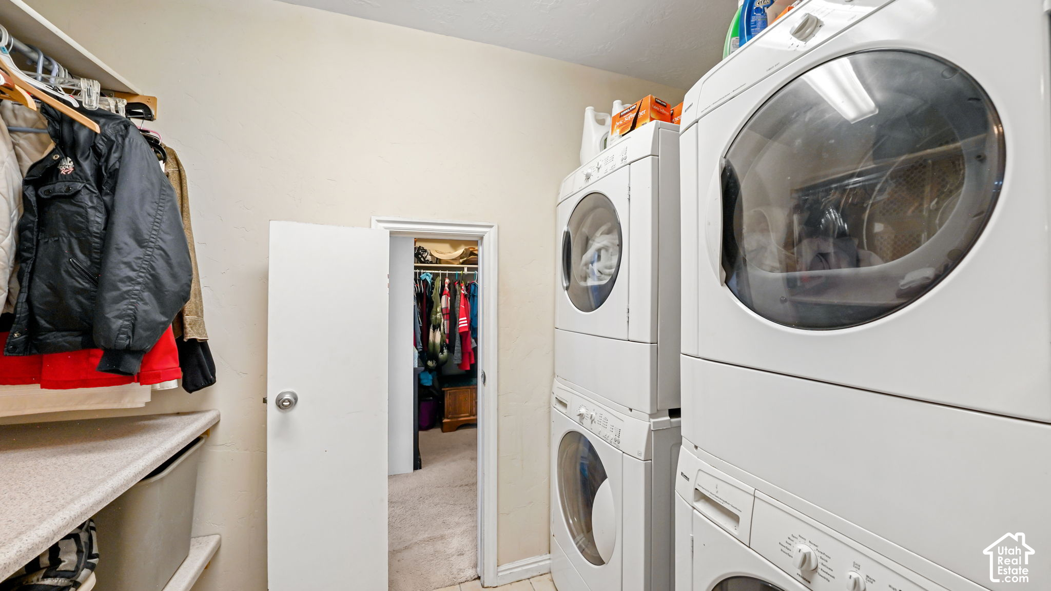 Laundry room with stacked front-loading machines, a countertop, and an open closet doorway.