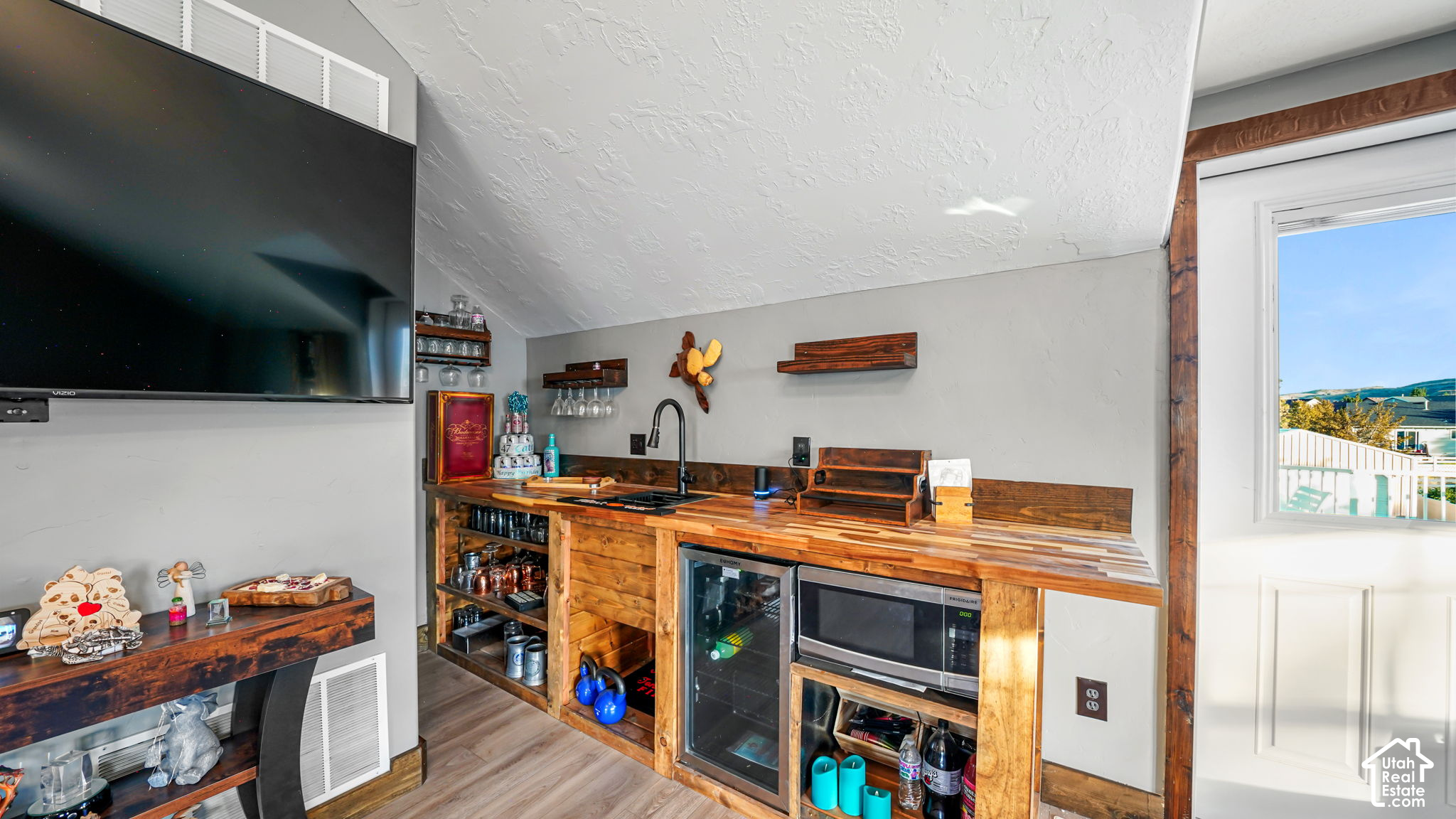 Basement wet bar with wood counters, beverage refrigerators, and a wall-mounted television.