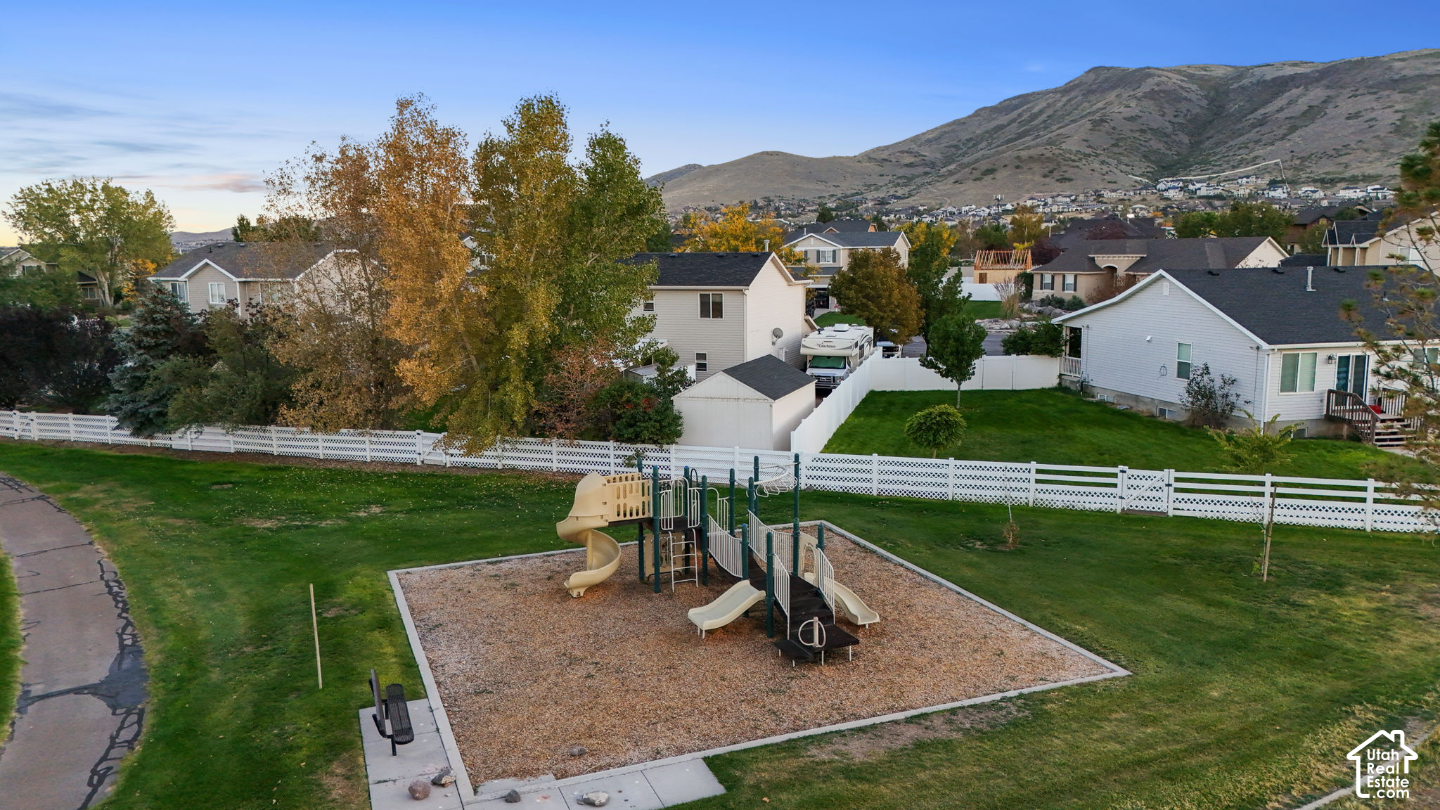Neighborhood playground and grassy common area with homes and mountains beyond.