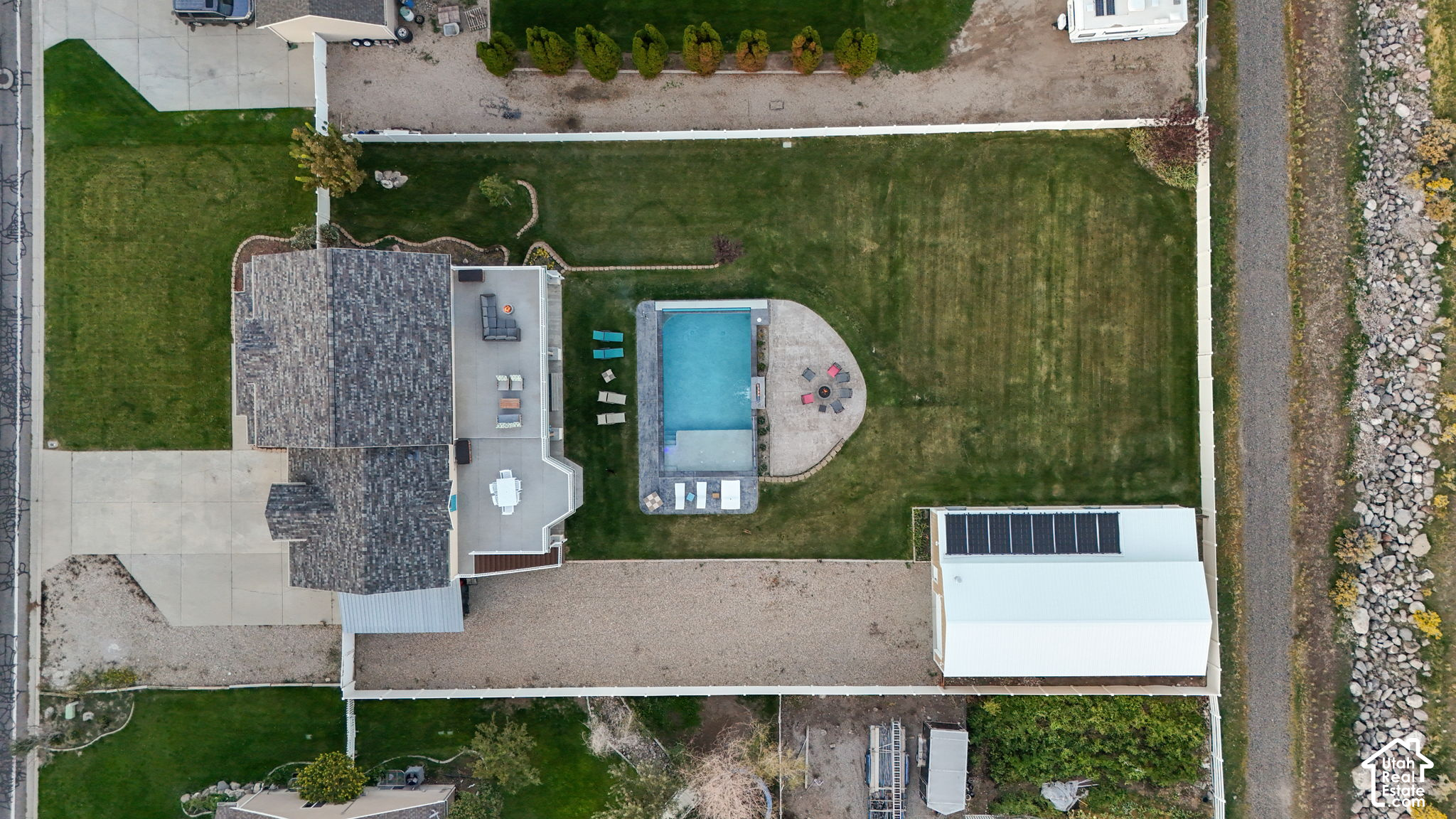 Aerial view of a home with a fenced lawn, swimming pool, patio, and detached outbuilding.