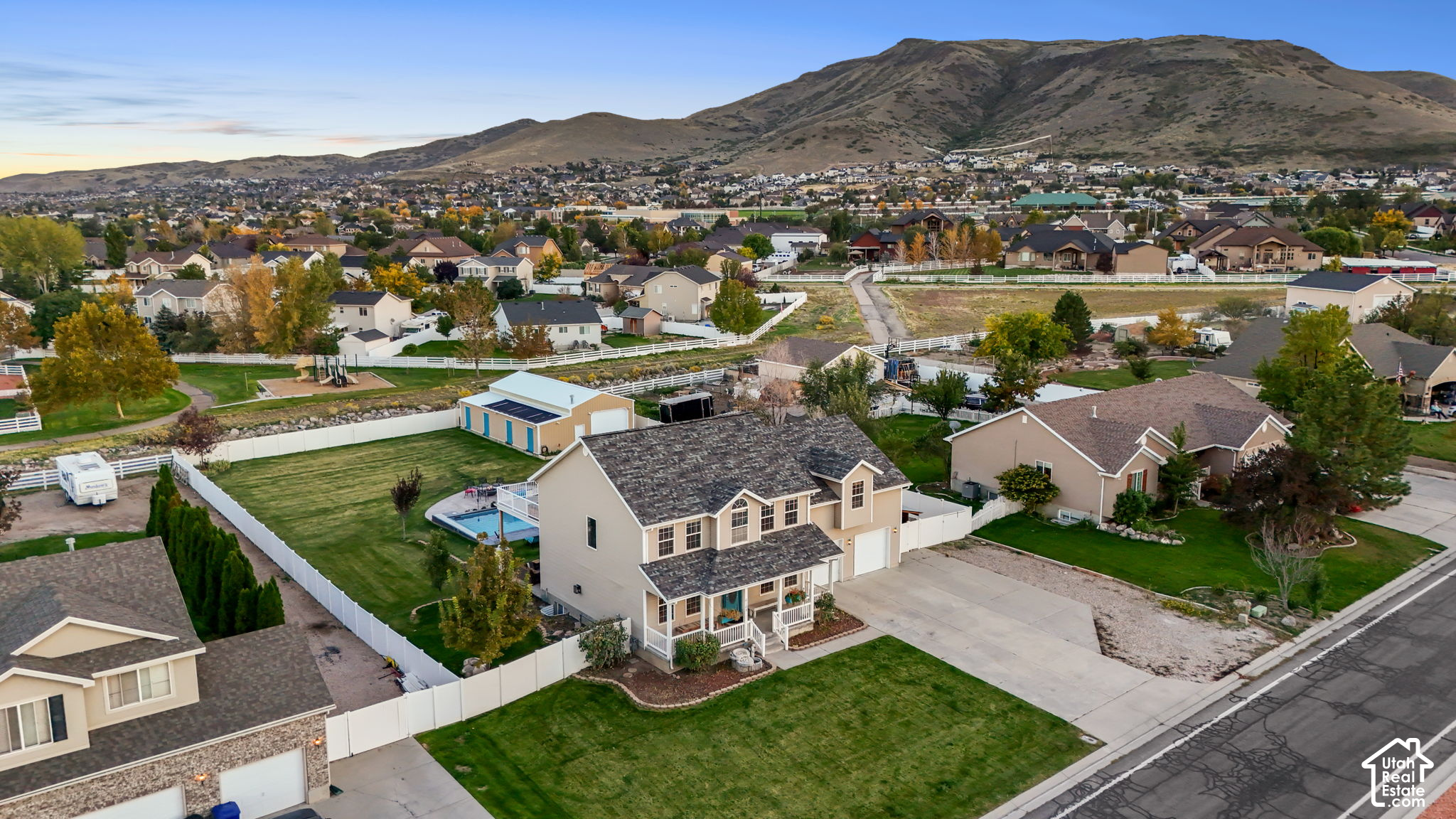 Aerial view of a home with a fenced yard and pool, neighboring homes, and a mountain backdrop.