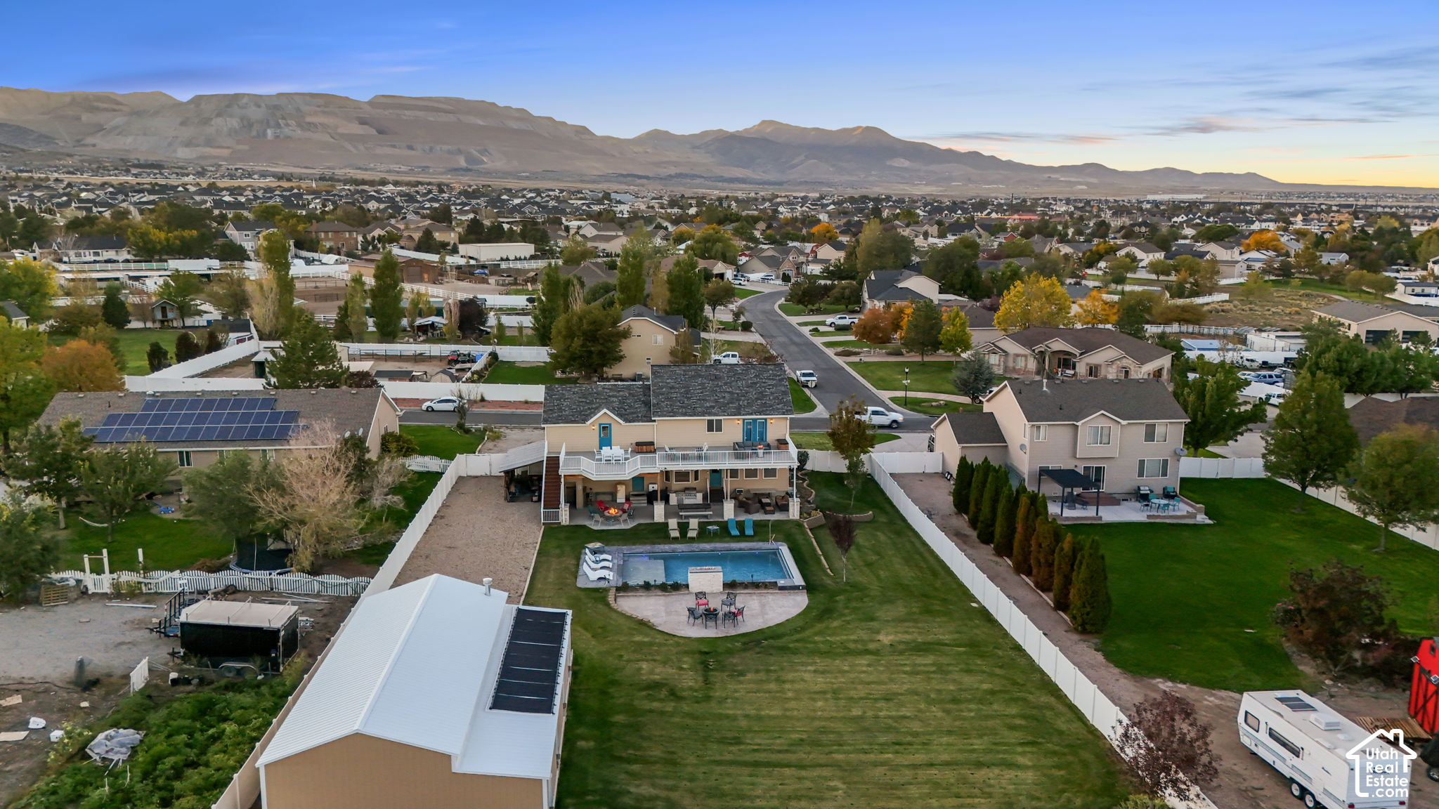 Aerial view of a Herriman home with a fenced pool and patio, surrounded by homes and foothills.