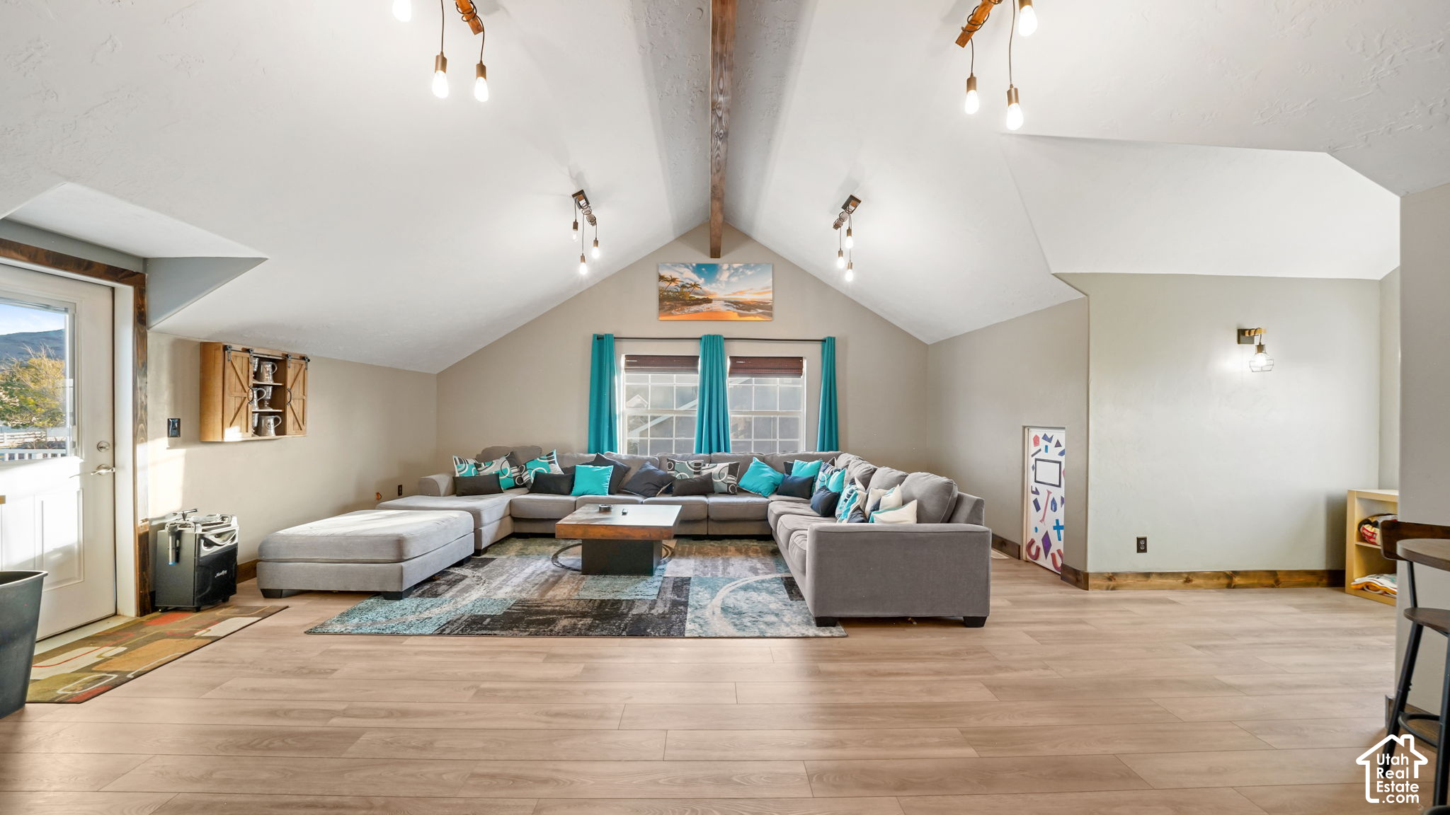 Furnished living room with vaulted ceiling, exposed wood beam, and gray sectional with teal pillows.