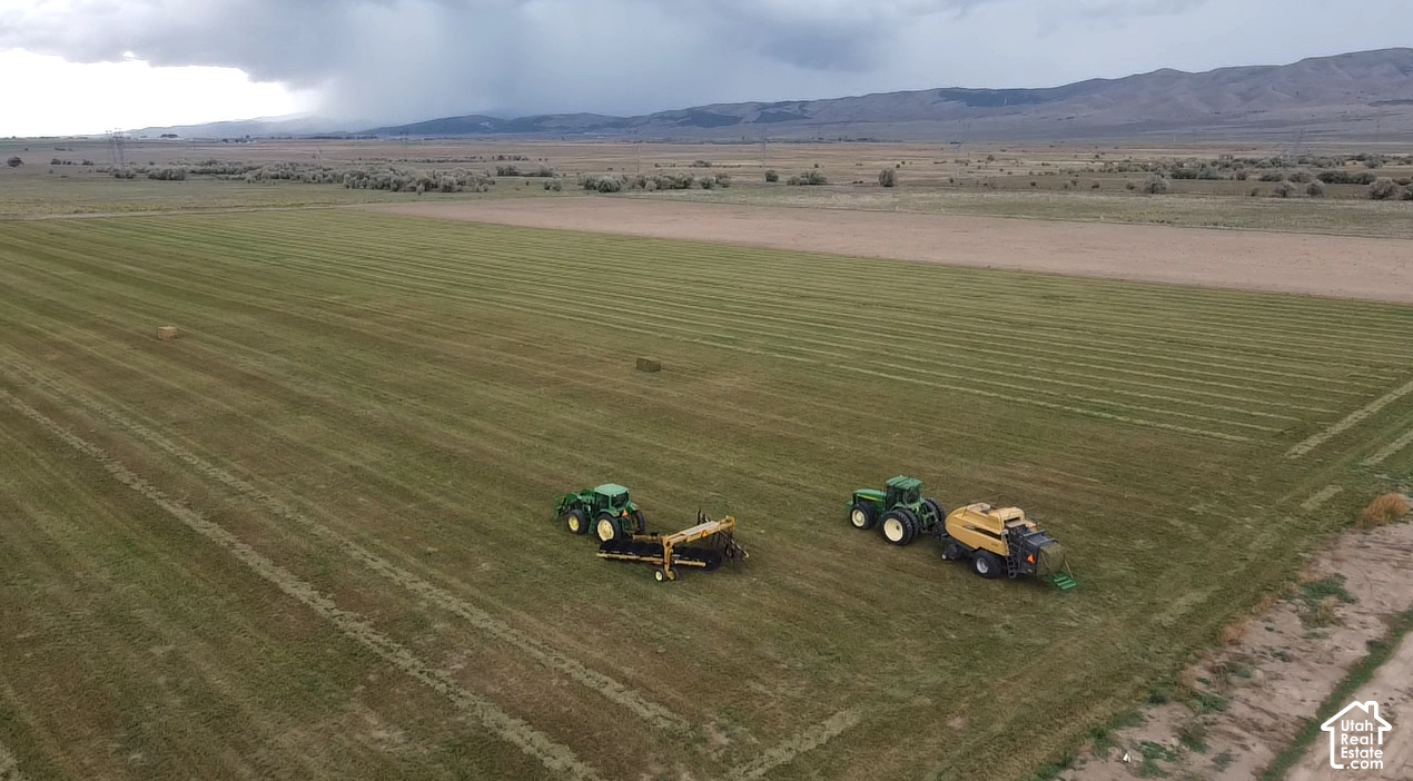 Aerial view of a mown field with two tractors and mountain ridges in the distance.