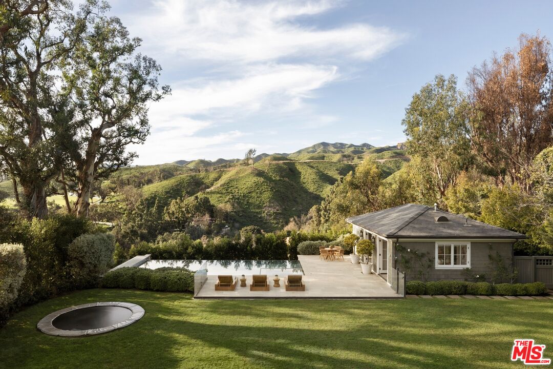 Home with a pool, circular spa, and furnished patio overlooking rolling green hills.