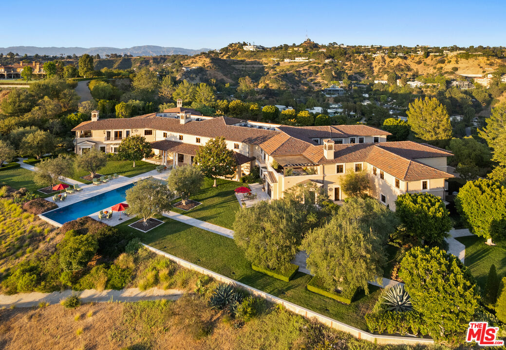 Aerial view of a sprawling Mediterranean-style estate with a long pool and landscaped grounds among rolling hills.