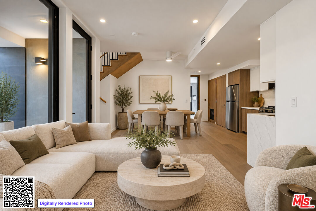 Open-plan living room, dining area, and kitchen with neutral furnishings, wood cabinetry, and an open staircase.