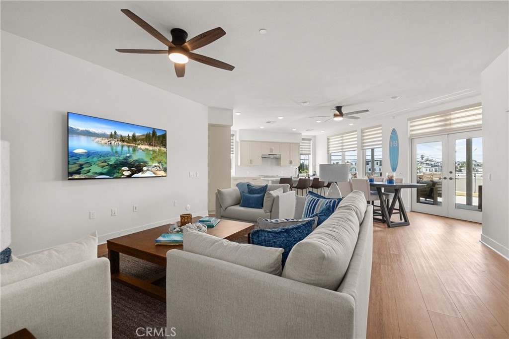 Open-plan living room with white sofas, blue accents, and dining area beside glass balcony doors.