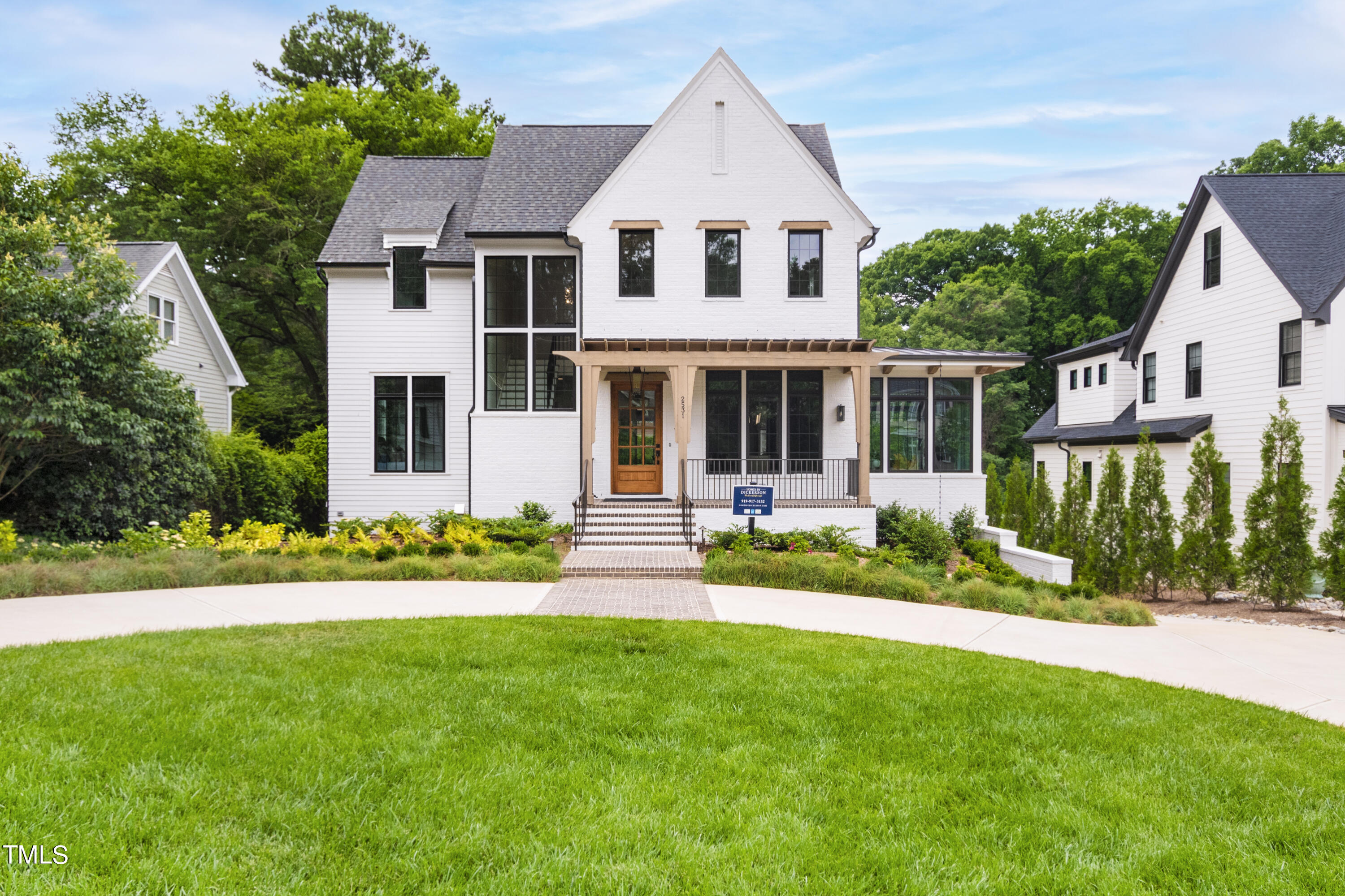 White two-story house with steep gables, a timber porch, brick steps, and a broad green lawn.